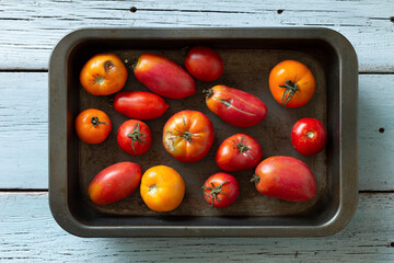 Ugly tomatoes in in an iron tray on a light wooden table, top view