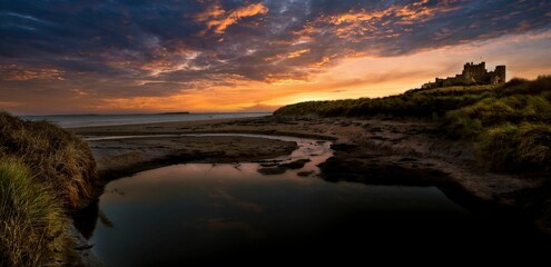 Beautiful shot of bright sunset sky over sea with Bamburgh Castle in distance in Northumberland ,UK