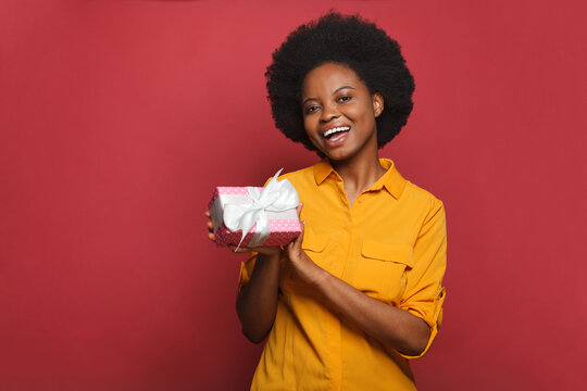 Happy woman holding gift box and smiling on red background