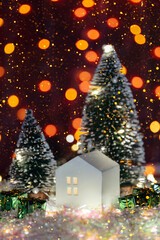 Christmas cute little house with tree in snow. Glowing festive garland on dark background. Cozy atmosphere with home decor with selective focus. New Year card