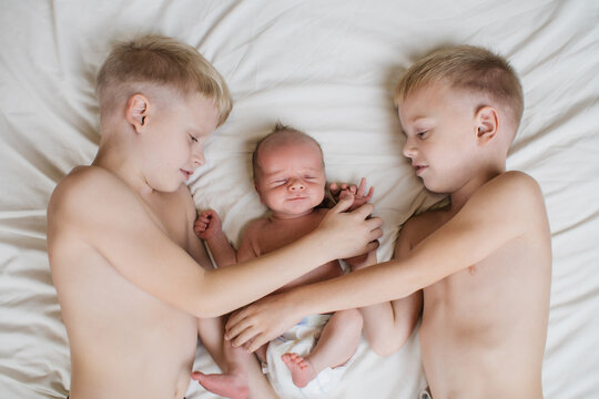three little cute brothers on the bed with white linen. High quality photo