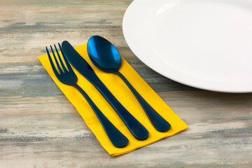 Blue fork knife and spoon on yellow napkin next to white plate