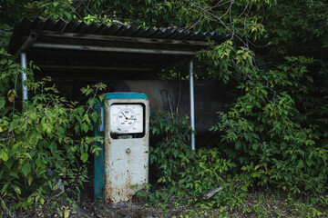 Old rusty abandoned gas station overgrown with grass and trees