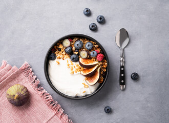 Natural yogurt with granola, berries and figs  in a bowl on a blue background. Healthy and...