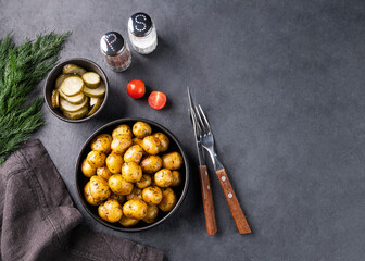 Fresh young roasted baby potatoes in a black pan with tomatoes and herbs on a dark  background.
