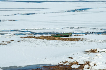 Old boat in a partially frozen lake. The boat is covered with snow