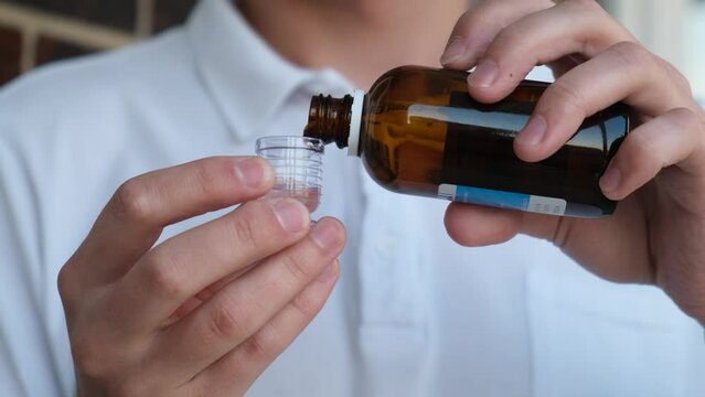 Unrecognizable man pouring a portion of cough syrup into the dispenser, close-up