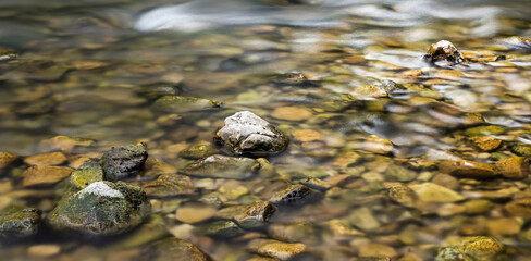 In focus stones diagonally on a calm riverbed. Warm tones, yellows and greens