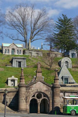 Fototapeta na wymiar Brooklyn, New York: A trolley waits for passengers below obelisks and mausoleums on a hillside in a section of historic Green-Wood Cemetery, founded in 1838.