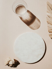 Marble white round podium, water glass. palm leaf and texture stone on beige background.
