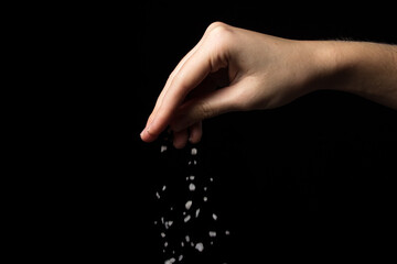 Coarse rock salt on a black background. Hand pours coarse salt