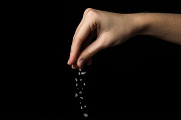 Coarse rock salt on a black background. Hand pours coarse salt