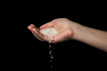 Coarse rock salt on a black background. Hand pours coarse salt