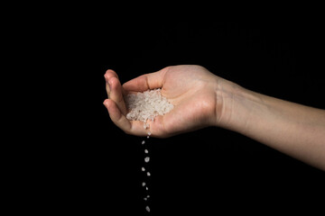 Coarse rock salt on a black background. Hand pours coarse salt