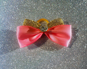 a pink and gold bow in the middle with a metal tab with stones lies on a silver shiny background. ...