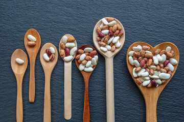 Beans in wooden spoons on black table, geometric progression concept