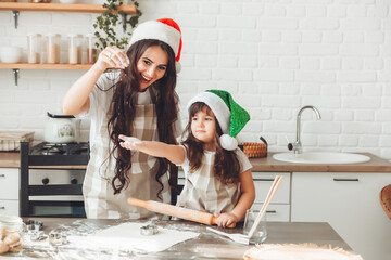 happy cheerful mother and child in Santa Claus hats are cooking Christmas cookies in the kitchen....