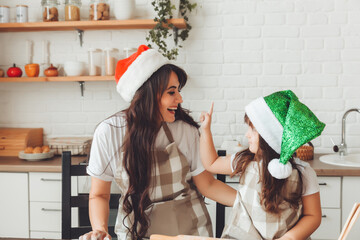 happy cheerful mother and child in Santa Claus hats are cooking Christmas cookies in the kitchen....