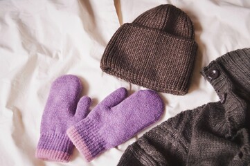 Handmade knitted cardigan, brown woolen hat and purple gloves. Autumn and winter comfy clothes. Warm clothing flat lay photo