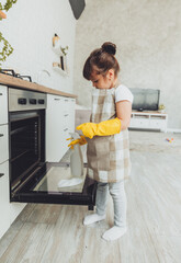 A little brunette girl wipes the oven in the kitchen at home. cleaning the kitchen. a child can...