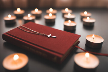 Silver christian cross on red paper bible book on table over burning candles close up