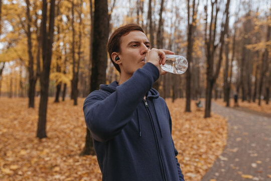 Concentrated sportsman drinking water during workout break in autumn park