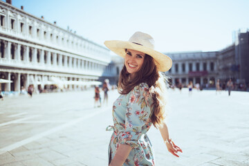 smiling trendy woman in floral dress with hat having excursion