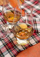 Tulip-shaped tasting glass with dram of Scotch single malt or blended whisky on wooden table with tartan