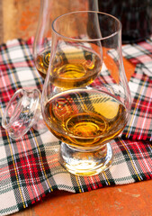 Tulip-shaped tasting glass with dram of Scotch single malt or blended whisky on wooden table with tartan