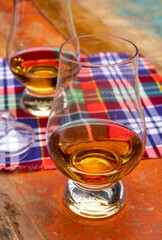 Tulip-shaped tasting glass with dram of Scotch single malt or blended whisky on wooden table with tartan