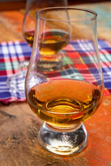 Tulip-shaped tasting glass with dram of Scotch single malt or blended whisky on wooden table with tartan