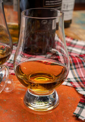 Tulip-shaped tasting glass with dram of Scotch single malt or blended whisky on wooden table with tartan