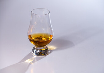 Tulip-shaped tasting glass with dram of Scotch single malt or blended whisky on white background