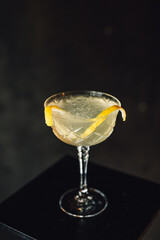 fancy yellow cocktail champagne crystal coupe lemon on pedestal against dark metal 