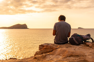 A tourist sitting watching the sunset at Cala Comte beach on the island of Ibiza. Balearic