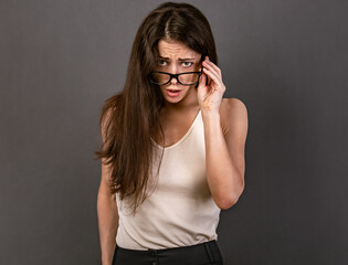 Angry serious surprising business woman with open big funny eyes in glasses holding the hand the eyeglasses in white t- shirt on empty copy space grey background. Closeup