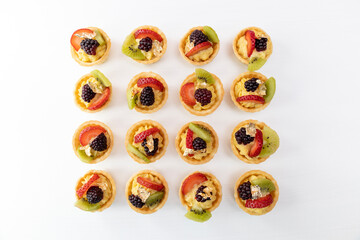 arranged in rows delicious cupcakes with cream and fruits as decoration, top perspective in studio, gourmet food with white background