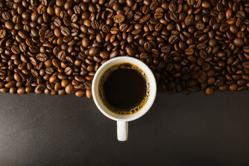 Coffee beans on a black background with a white cup.