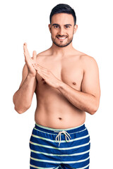 Fototapeta premium Young handsome man wearing swimwear clapping and applauding happy and joyful, smiling proud hands together