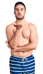 Fototapeta premium Young handsome man wearing swimwear looking at the camera blowing a kiss with hand on air being lovely and sexy. love expression.