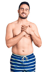Fototapeta premium Young handsome man wearing swimwear smiling with hands on chest with closed eyes and grateful gesture on face. health concept.