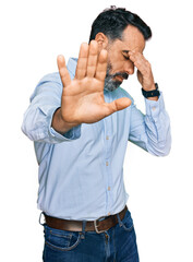 Middle aged man with beard wearing business shirt covering eyes with hands and doing stop gesture with sad and fear expression. embarrassed and negative concept. - obrazy, fototapety, plakaty
