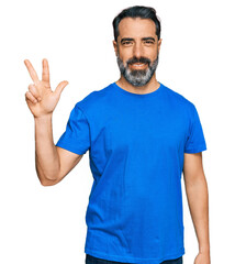 Middle aged man with beard wearing casual blue t shirt showing and pointing up with fingers number three while smiling confident and happy.