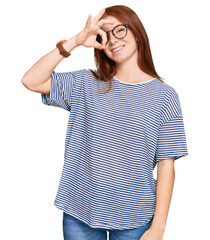 Young read head woman wearing casual clothes and glasses doing ok gesture with hand smiling, eye...