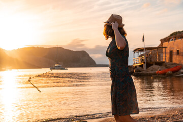 Fototapeta premium A young woman with a hat walking along the Benirras beach in Ibiza, sunset. vacation concept