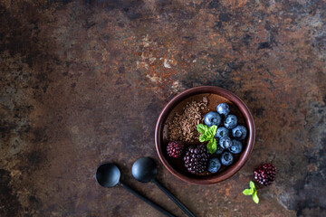 Three ramekins with chocolate mousse with blueberries, blackberries and fresh mint on a rusty iron background.