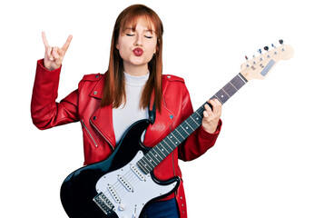 Fototapeta premium Redhead young woman playing electric guitar doing rock gesture looking at the camera blowing a kiss being lovely and sexy. love expression.