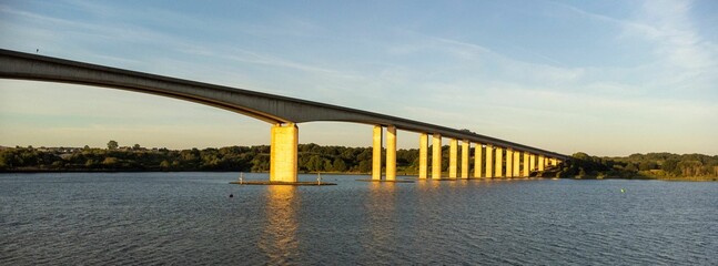 Low-angle of a sunlit Orwell bridge at sunset, a cloudy sky and cityscape background