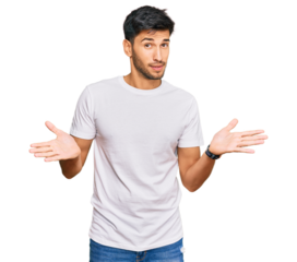Young handsome man wearing casual white tshirt clueless and confused expression with arms and hands raised. doubt concept.