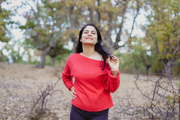 portrait of a beautiful woman in the countryside wearing a red blouse touching her hair and looking at the camera